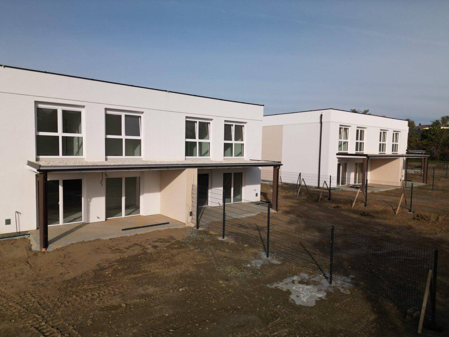Zwei moderne Reihenhäuser in der Bauphase mit großen Fenstern und zukünftigen Terrassen.