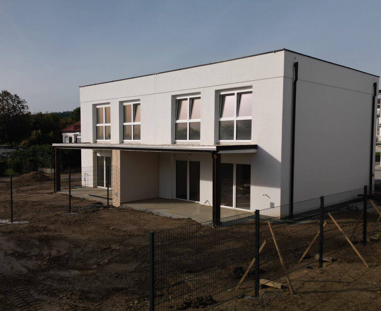 Weißes Reihenhaus im Bau mit großzügigen Fensterflächen und vorbereitetem Terrassenbereich.