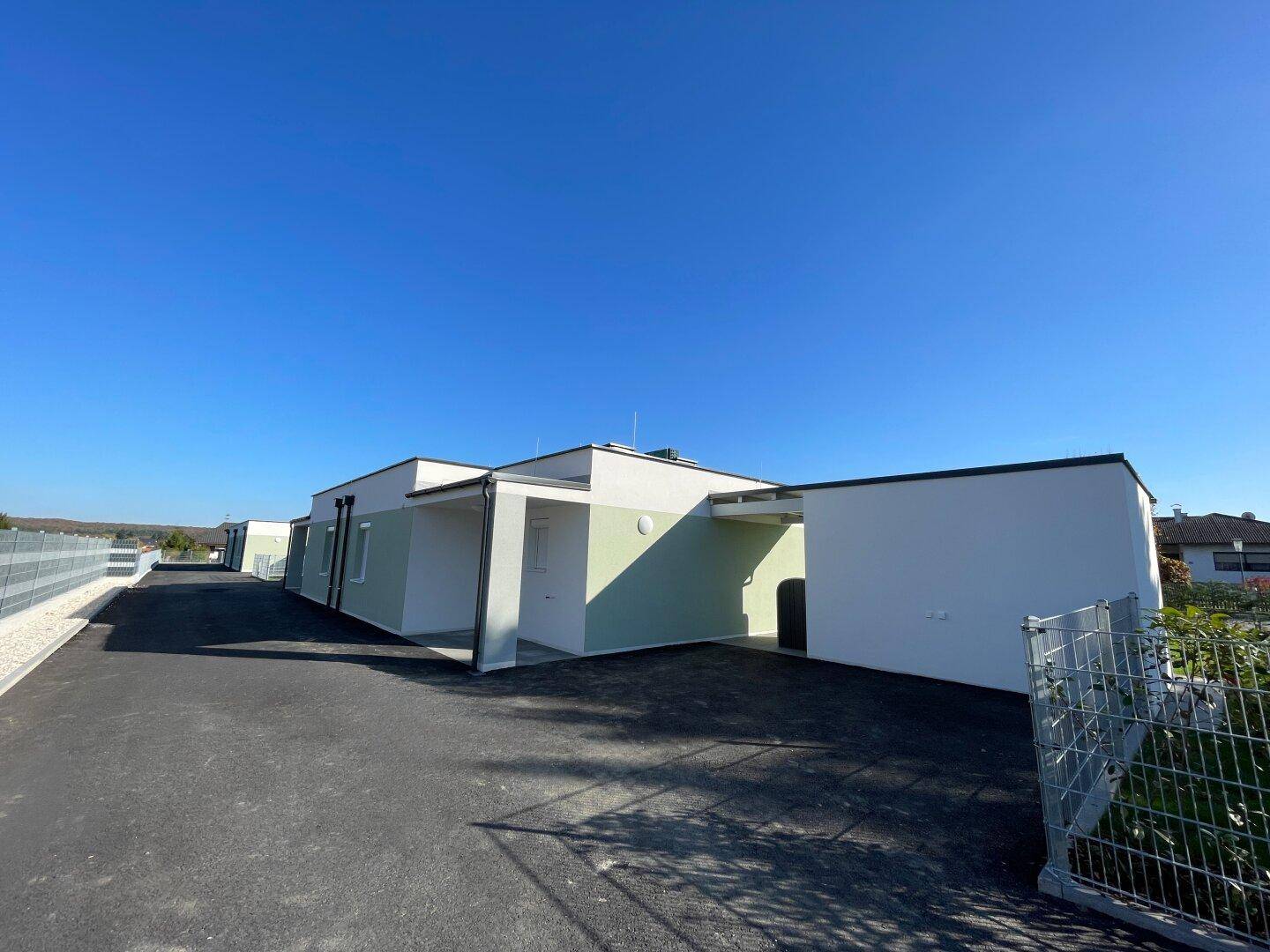 Reihe moderner Neubauten mit Carports und klarem Himmel, die eine neue Wohnsiedlung zeigen.