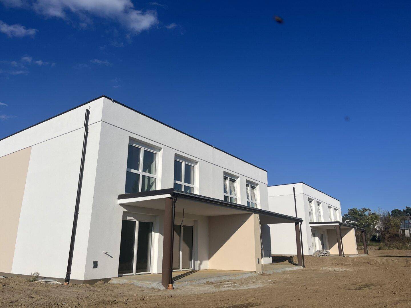 Neubau-Reihenhäuser mit klaren Linien und großen Fensterfronten unter blauem Himmel.