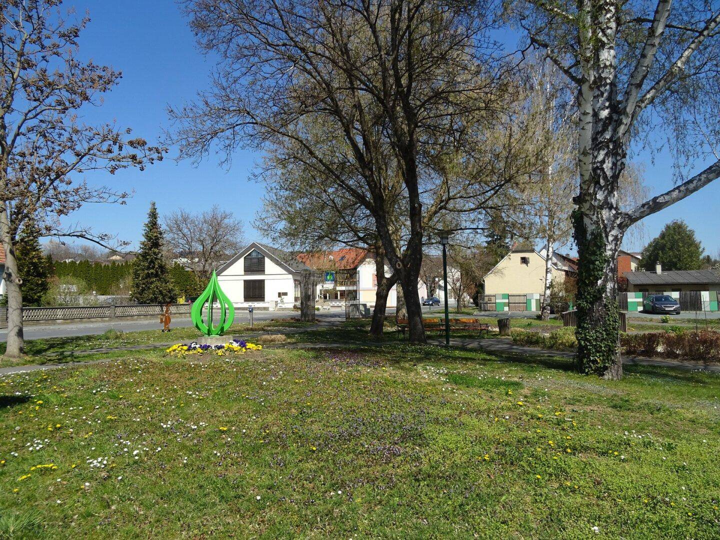 Grüne Parkanlage in der Nachbarschaft mit Bäumen und einem modernen Kunstobjekt.
