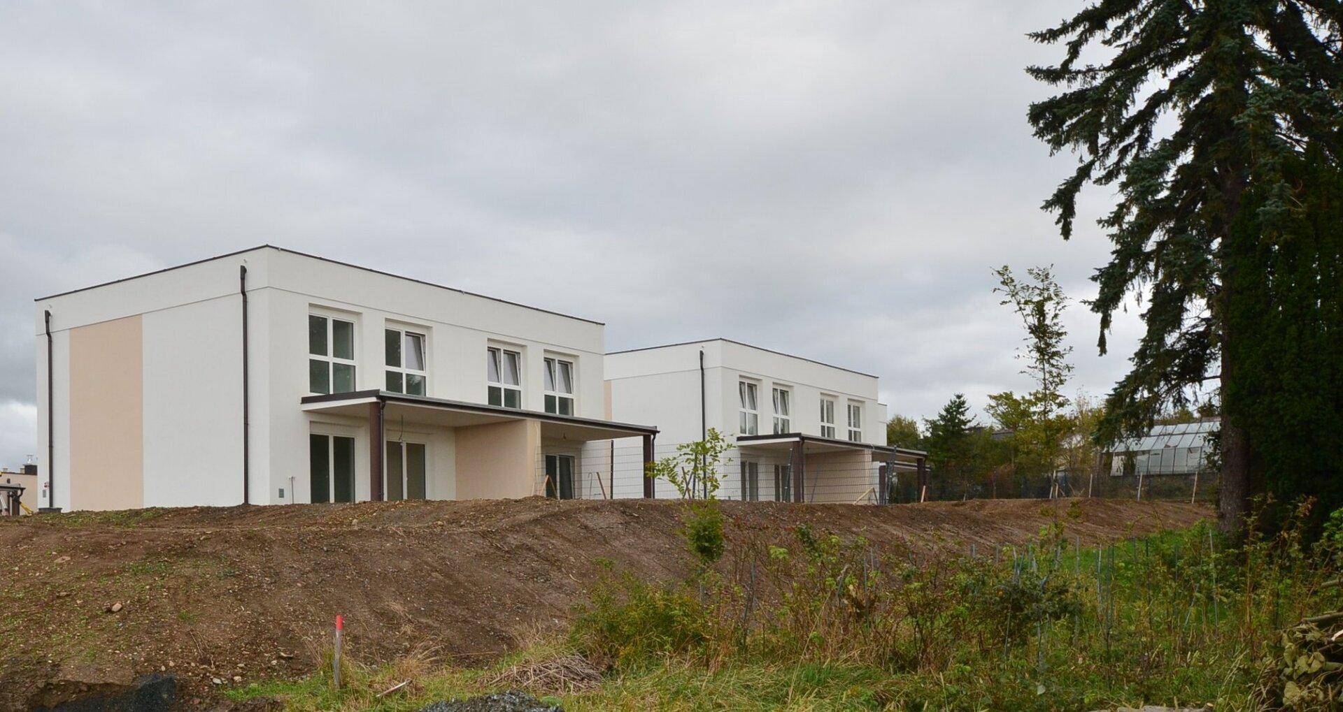 Rückansicht von Neubau-Reihenhäusern mit Terrassen und Blick auf unfertiges Gartengelände.