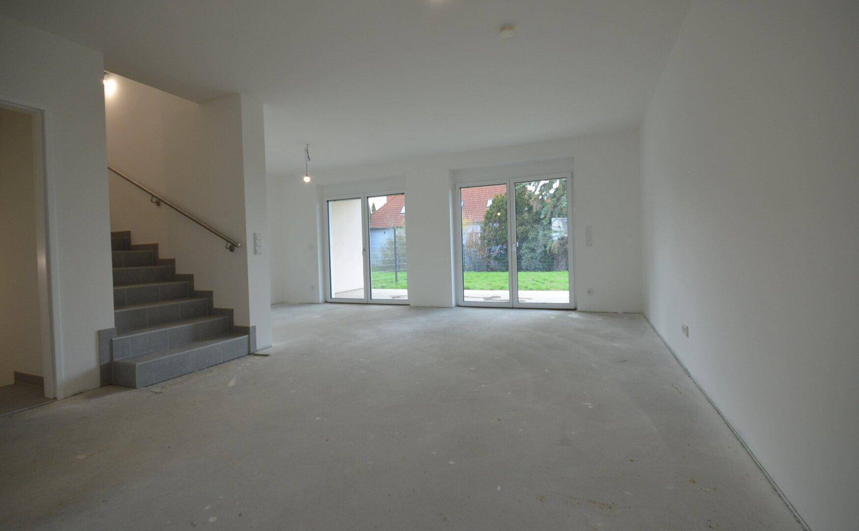 Geräumiger, heller Wohnbereich im Erdgeschoss mit großen Fenstern und Zugang zum Garten.