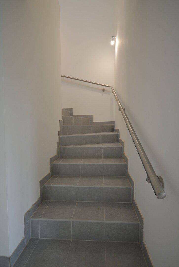 Treppenhaus mit gefliesten Stufen und einem schlichten Metallgeländer in modernem Design.