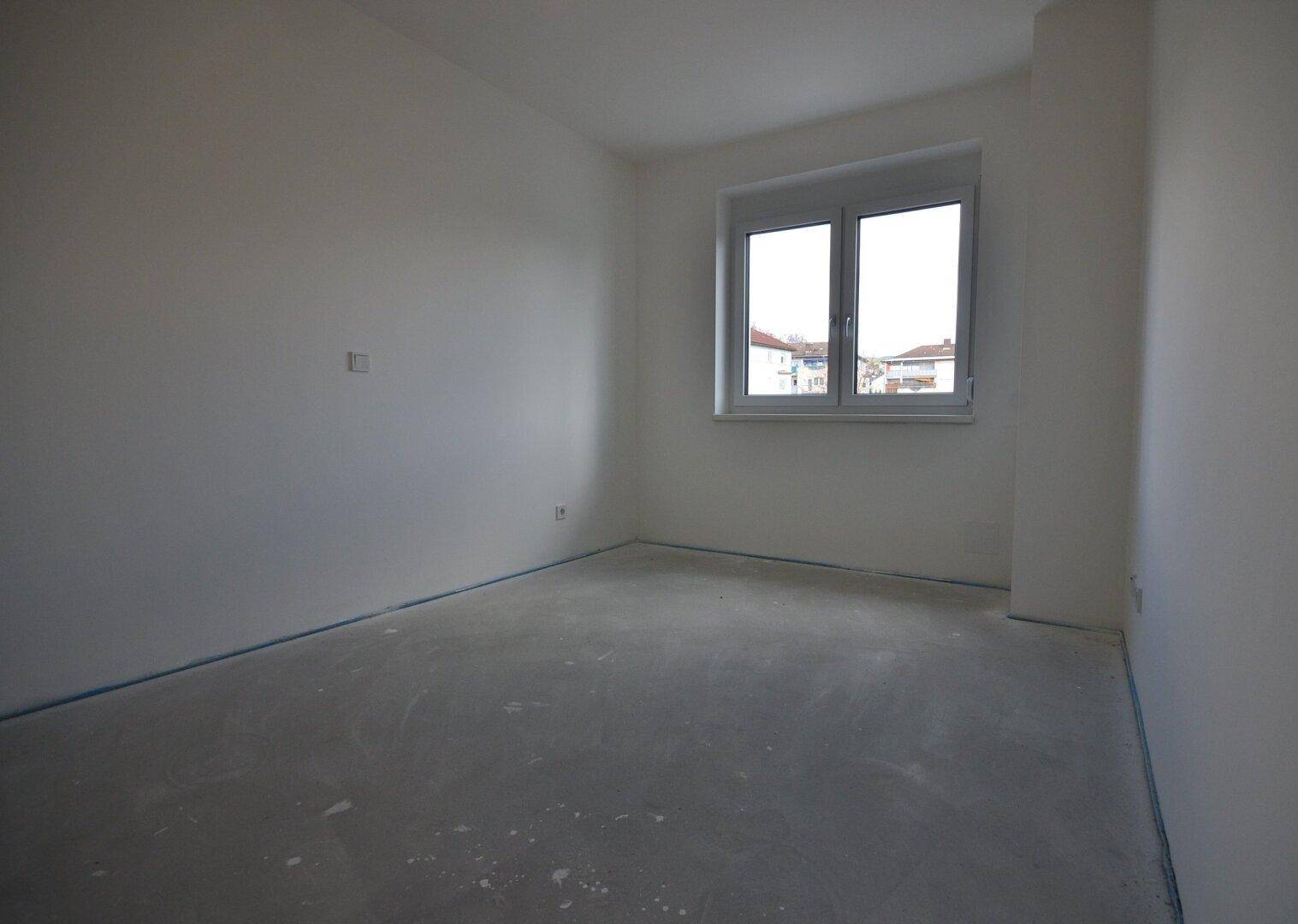 Helles Zimmer im Rohbauzustand mit einem Fenster und Blick auf die Nachbarschaft.