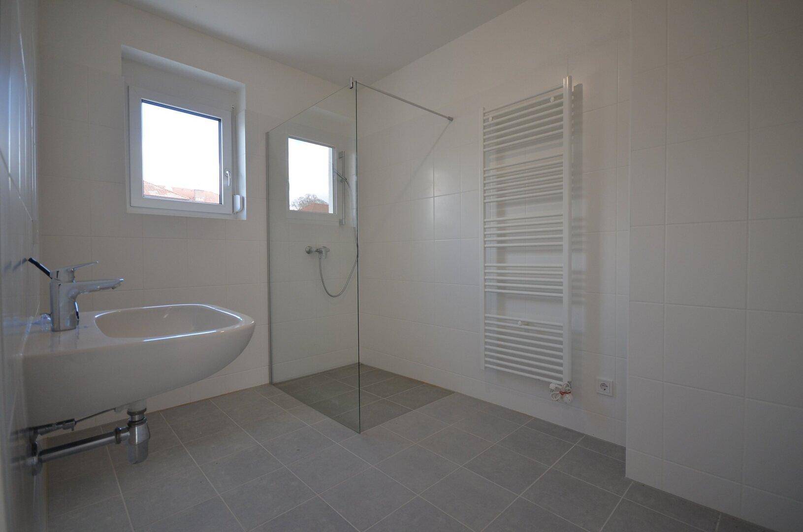 Modernes Badezimmer mit ebenerdiger Dusche, Waschbecken und beheiztem Handtuchhalter.