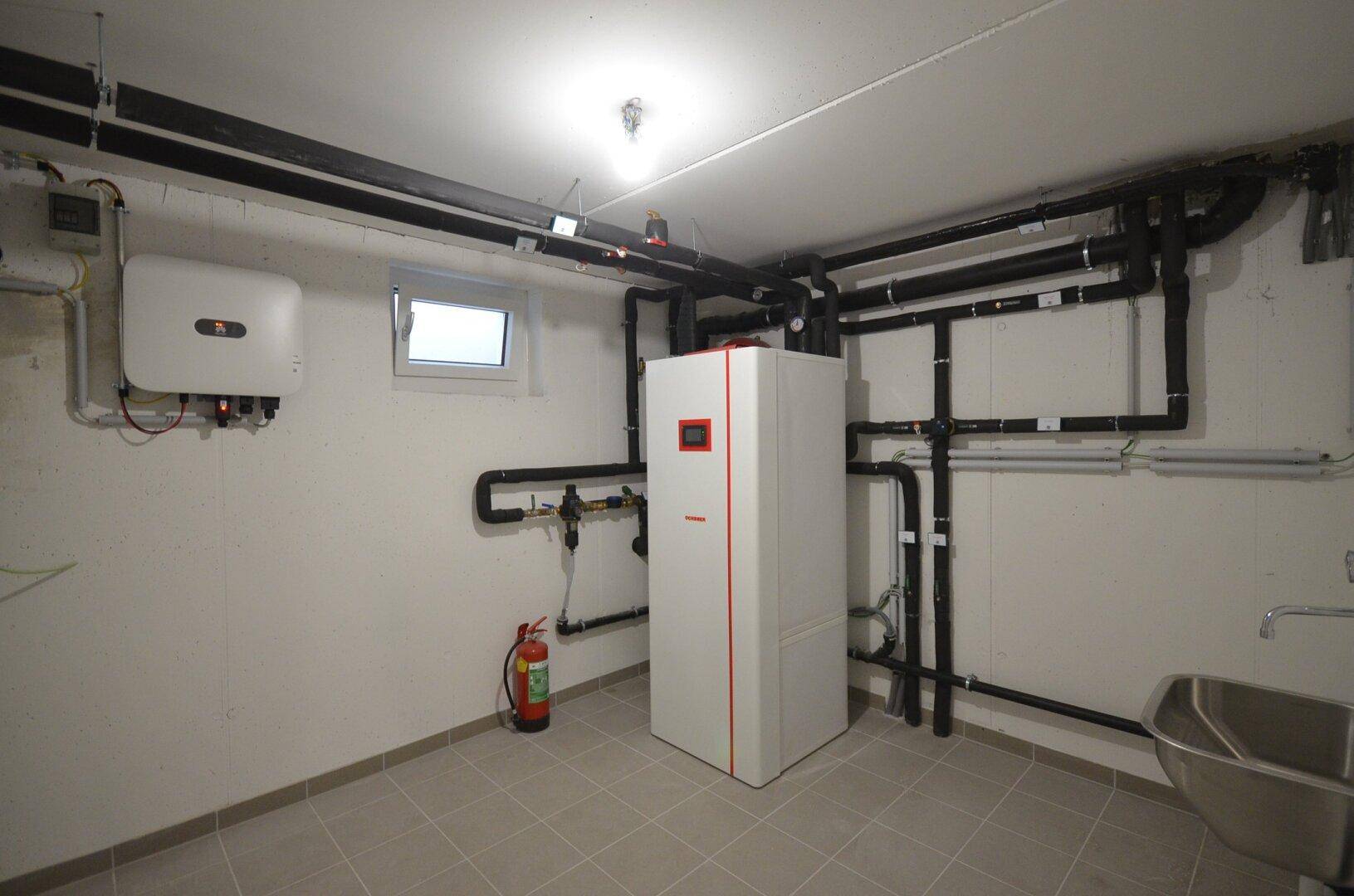 Technikraum im Keller mit Heizungsanlage, Rohren und einem kleinen Fenster.