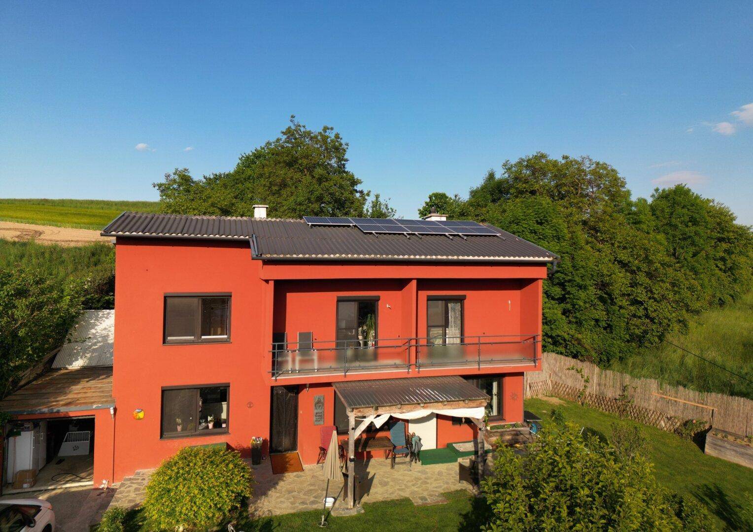 Rotes Wohnhaus mit zwei Balkonen, Solaranlage und einer überdachten Terrasse.