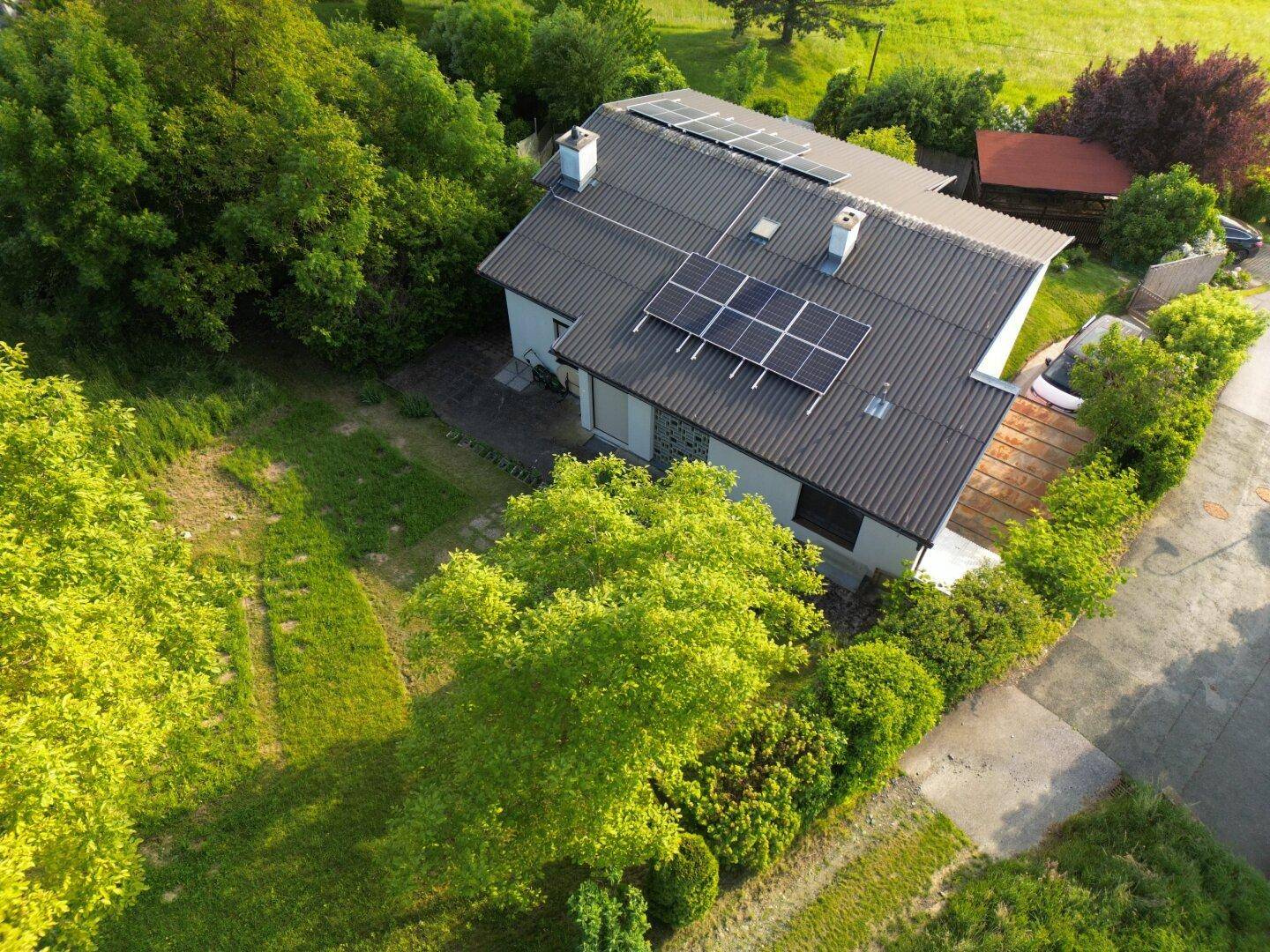 Luftaufnahme eines Hauses mit Solaranlage, umgeben von gepflegtem Garten und Bäumen.