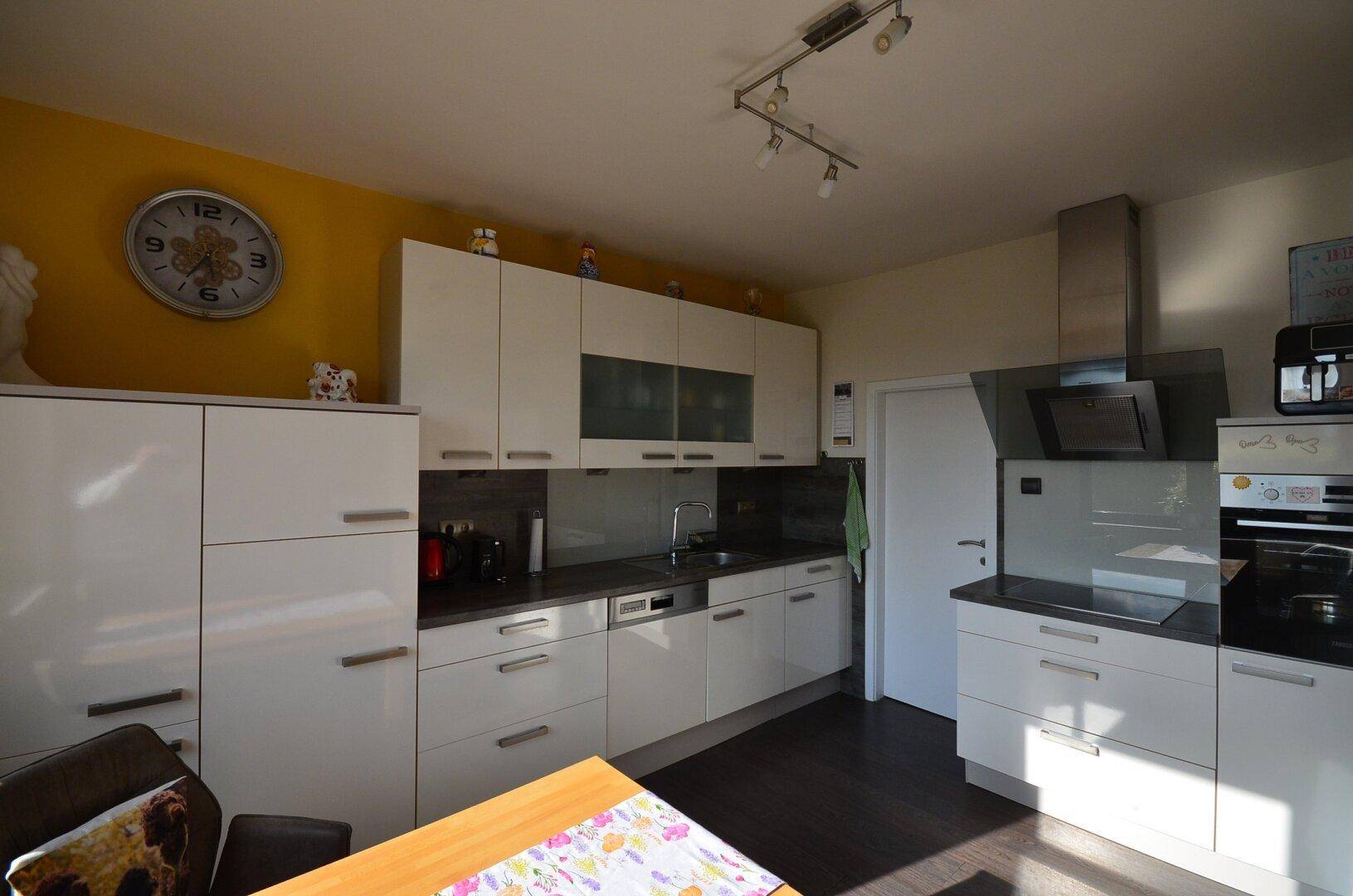 Moderne Küche mit weißen Hochglanzfronten, dunkler Arbeitsplatte und gelber Akzentwand.