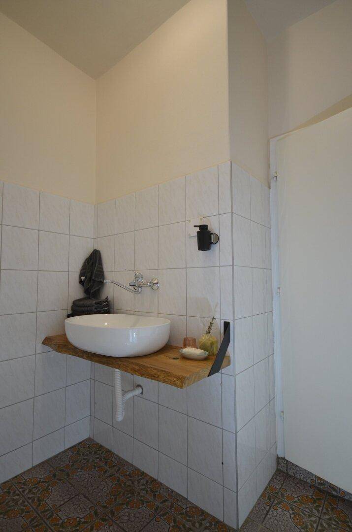 Modernes Gäste-WC mit Aufsatzwaschbecken auf Holzplatte und gemusterten Fliesen.