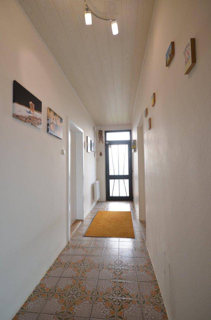Langer Flur mit gemusterten Fliesen, Bildern an der Wand und Eingangstür.