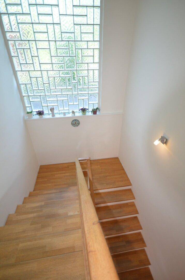 Holztreppe mit Geländer und einem großen, dekorativen Glasfenster im Treppenhaus.