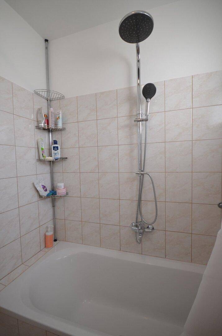 Badezimmer mit Badewanne und Duschvorrichtung, gefliesten Wänden und Duschablage.