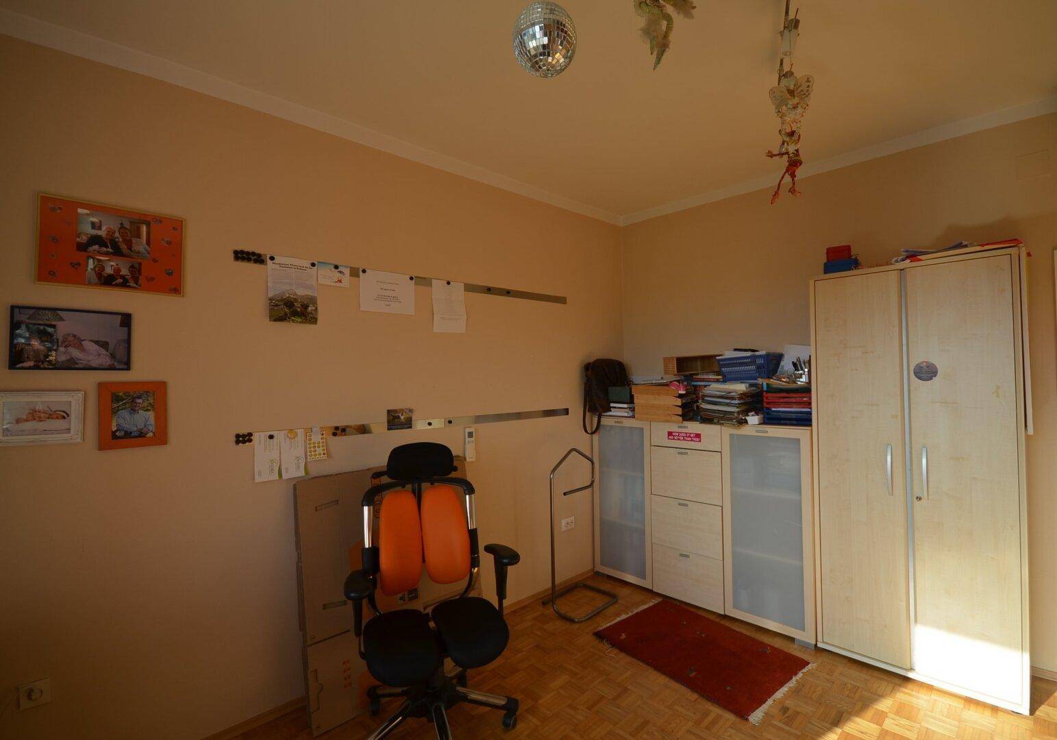 Schlafzimmer mit Parkettboden, Schränken und einem Bürostuhl.