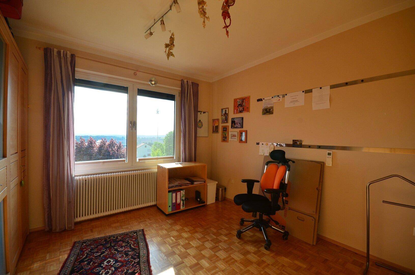 Helles Zimmer mit Parkettboden, großem Fenster und Blick ins Grüne.