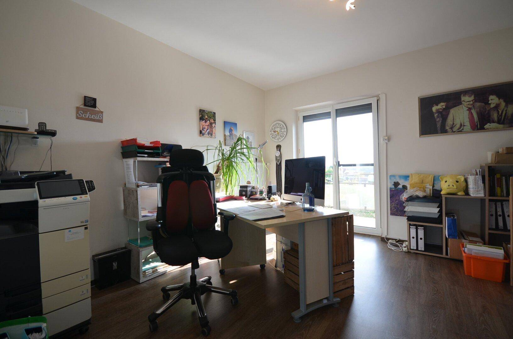 Geräumiges Arbeitszimmer mit Schreibtisch, Bürostuhl und Zugang zum Balkon.