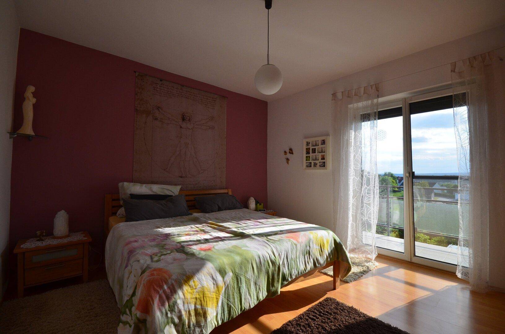 Helles Schlafzimmer mit Holzboden, einer Akzentwand und Zugang zu einem Balkon mit Aussicht.