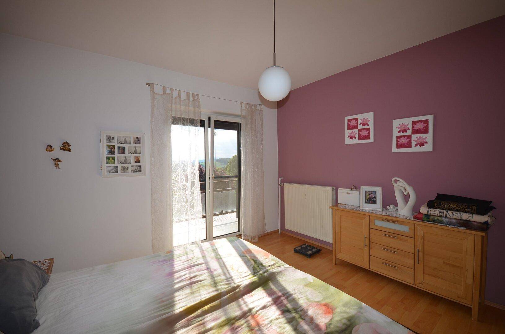 Schlafzimmer mit Holzboden, einer lila Akzentwand und einem Heizkörper unter dem Fenster.