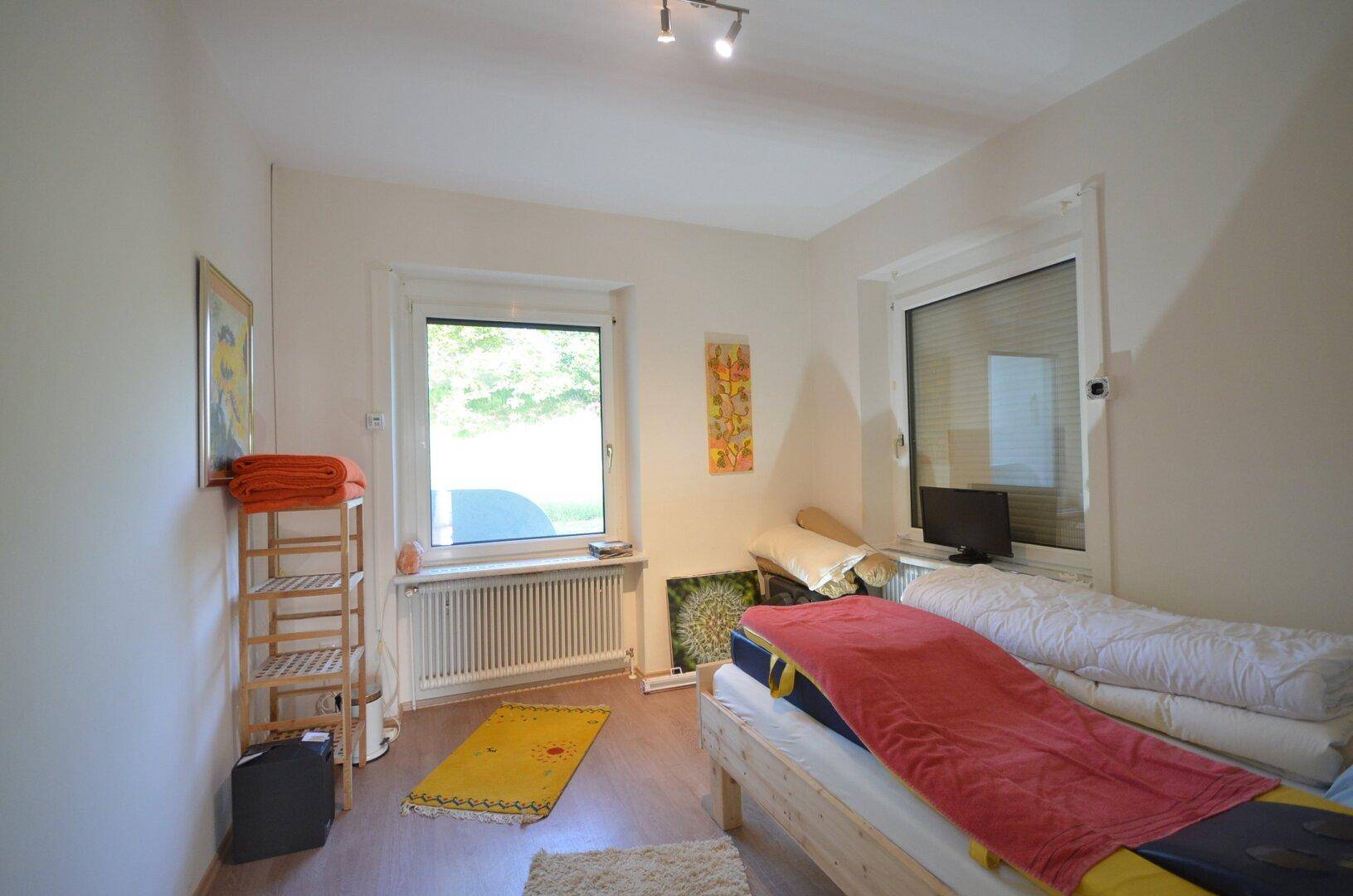 Einfaches Schlafzimmer mit zwei Betten, Holzboden und Blick ins Grüne durch die Fenster.