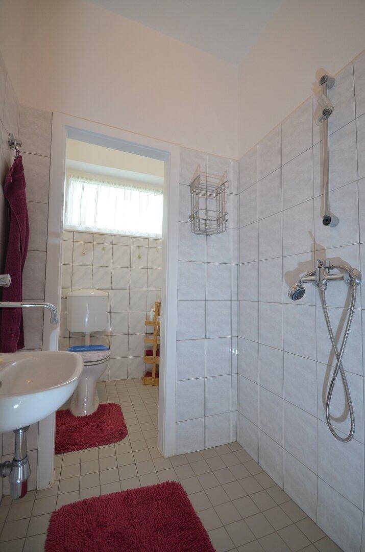 Badezimmer mit weißen Fliesen, einer Dusche und einem separaten WC-Bereich.