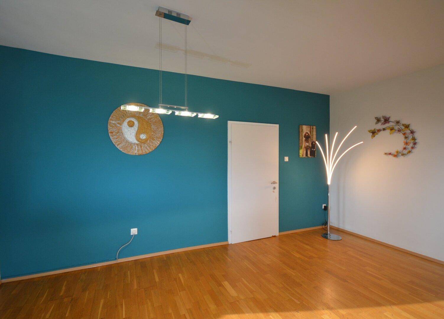 Geräumiges Wohnzimmer mit Holzboden und einer auffälligen blauen Akzentwand.