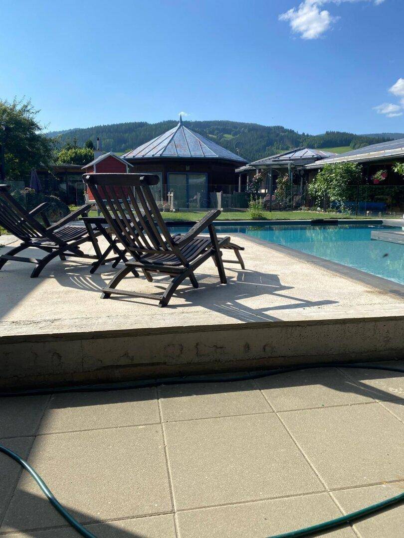 Sonniger Poolbereich mit Liegestühlen und einem malerischen Blick auf die umliegenden Berge.