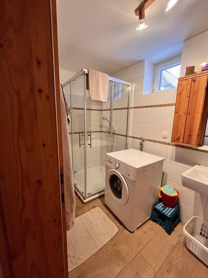 Badezimmer mit Duschkabine, Waschmaschine und Fliesenboden in funktionalem Design.
