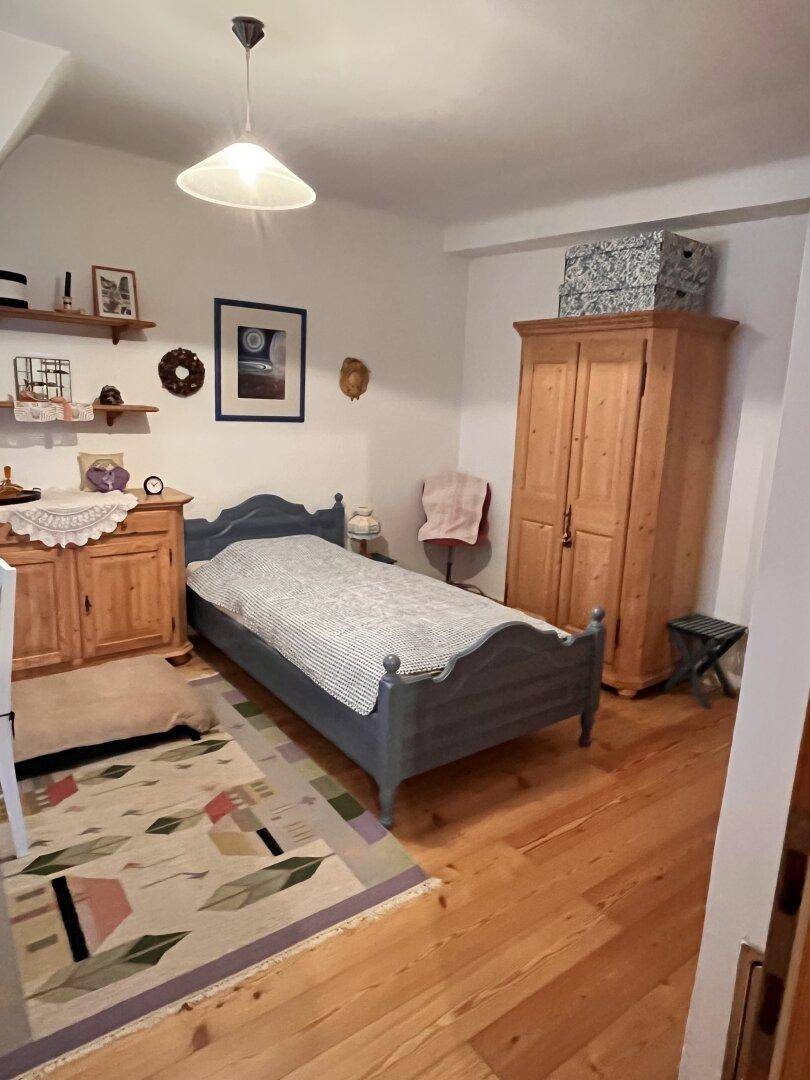 Schlafzimmer mit Holzboden, traditionellem Bett und Kleiderschrank in hellem Ambiente.