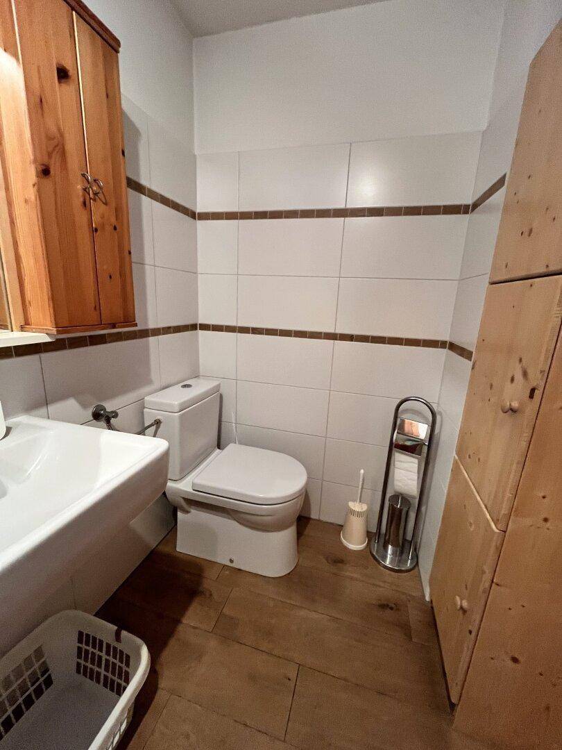 Separate Toilette mit Waschbecken, WC und Holzschrank in schlichtem Design.