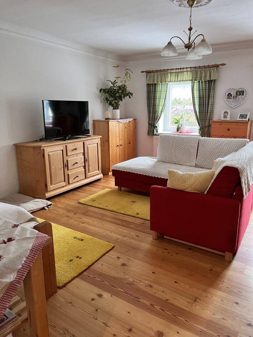 Gemütliches Wohnzimmer mit Holzboden, rotem Sofa und Fernseher, hell und einladend.