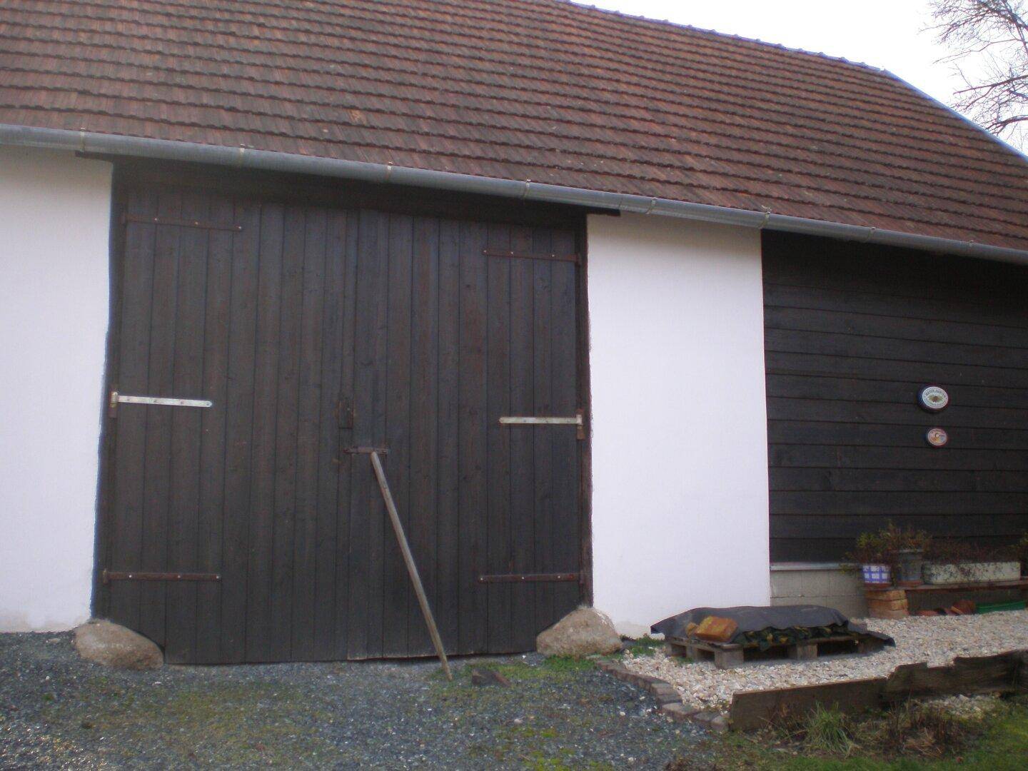 Große Holztore einer Scheune oder Garage mit weißer Fassade und Ziegeldach.