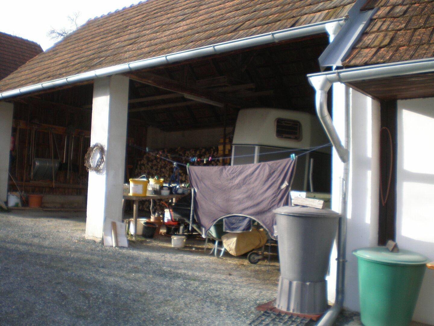 Überdachter Außenbereich mit Lagerung von Holz und verschiedenen Gegenständen.
