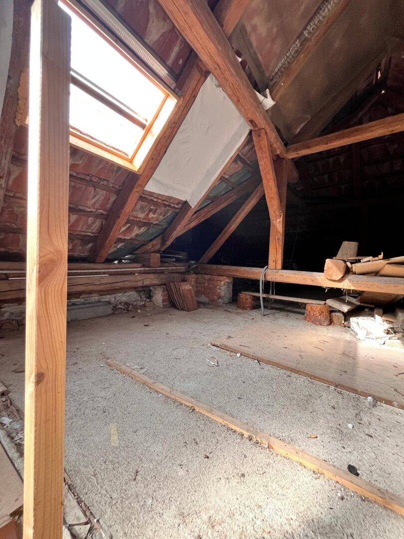 Unausgebauter Dachboden mit sichtbaren Holzbalken und Dachfenster für natürliches Licht.