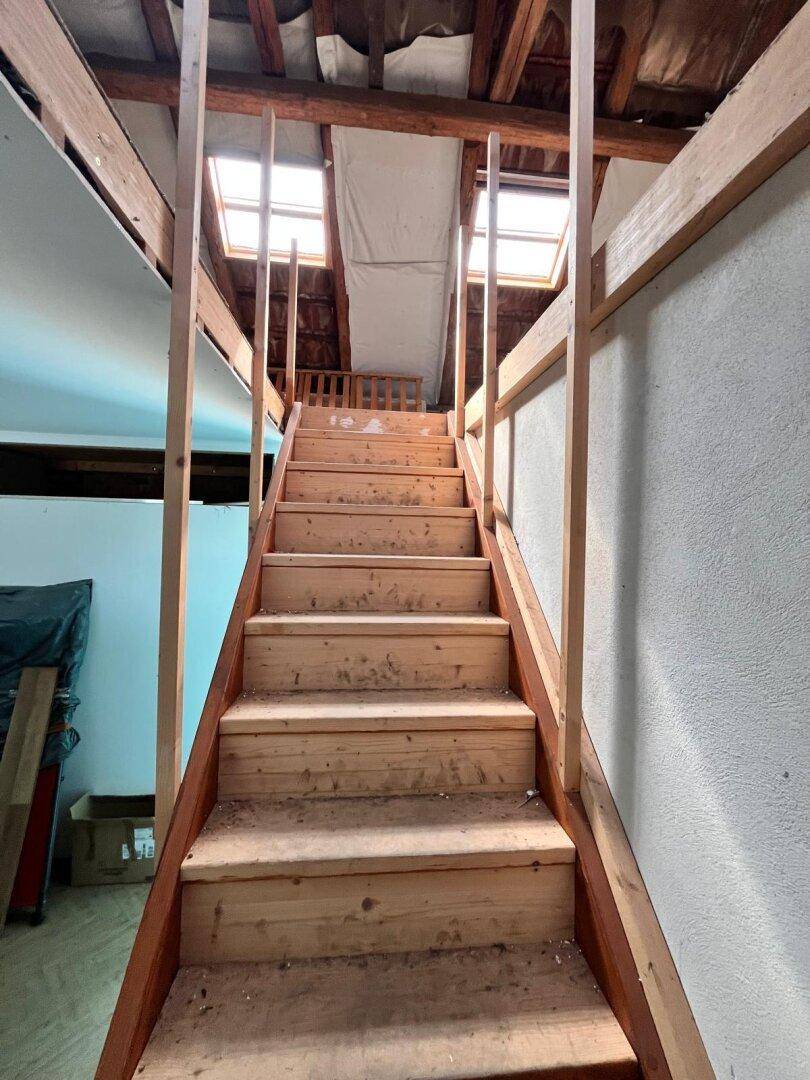 Holztreppe führt hinauf zum Dachboden mit zwei Dachfenstern, die den Raum erhellen.
