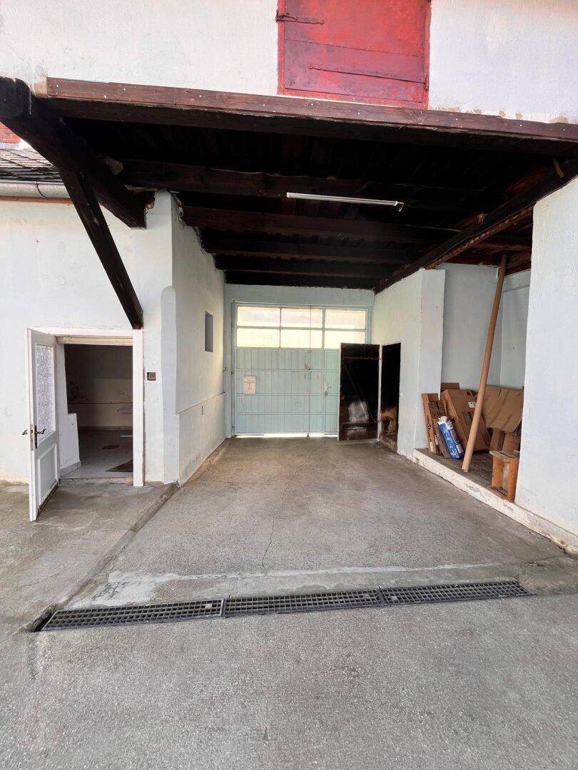 Überdachter Garagenbereich mit Rolltor und Zugang zu weiteren Räumen.