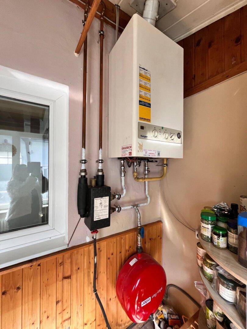 Hauswirtschaftsraum mit Gastherme, Warmwasserspeicher und Holzverkleidung an der Wand.