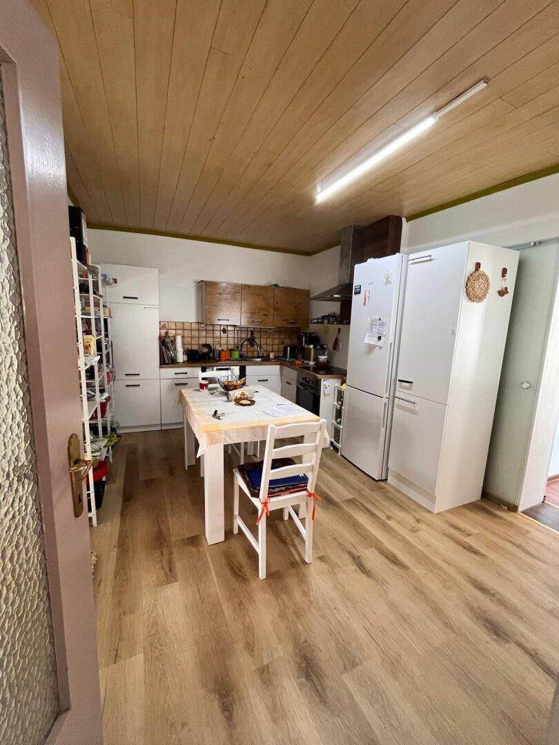 Geräumige Küche mit weißen Schränken, Esstisch und Holzpaneeldecke.