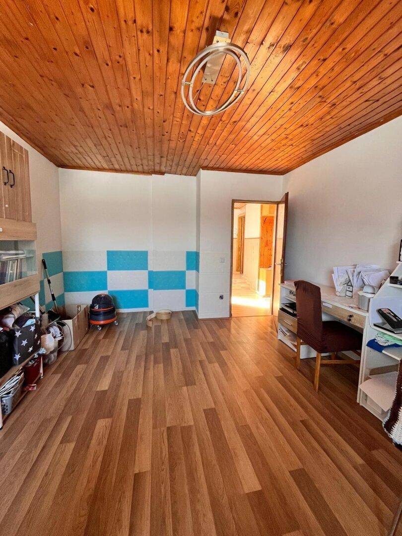 Zimmer mit Holzbalkendecke, Laminatboden und einer Wand mit blau-weißem Muster.