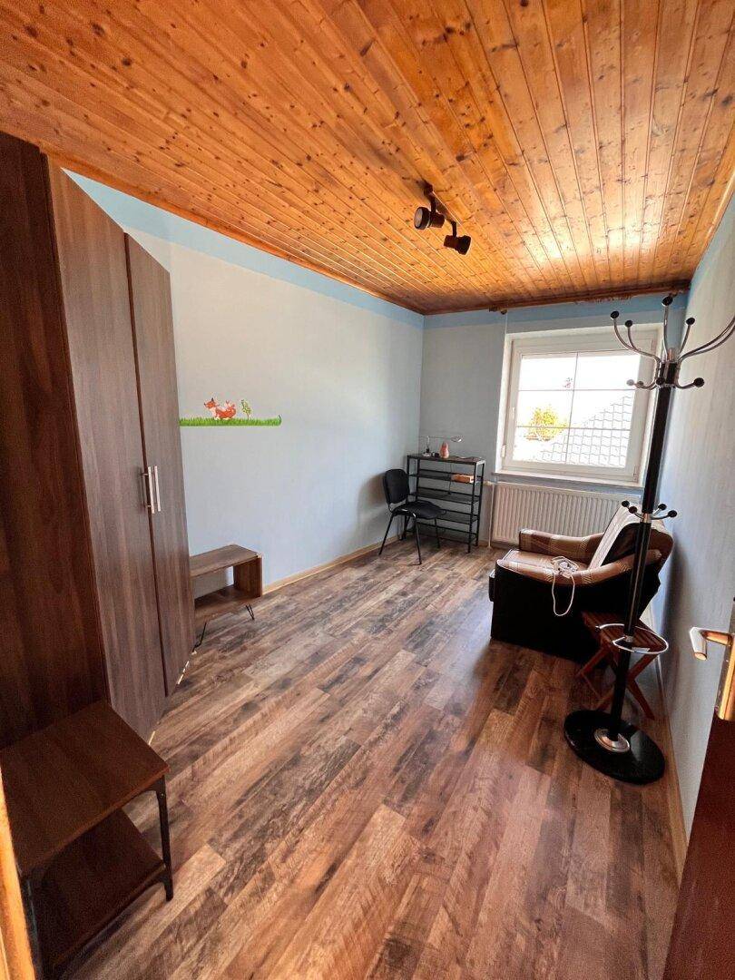 Schlafzimmer mit Holzbalkendecke, Laminatboden und einem Fenster mit Blick nach draußen.