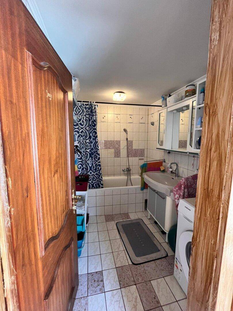 Badezimmer mit Badewanne, Waschbecken und Fliesen in verschiedenen Mustern.