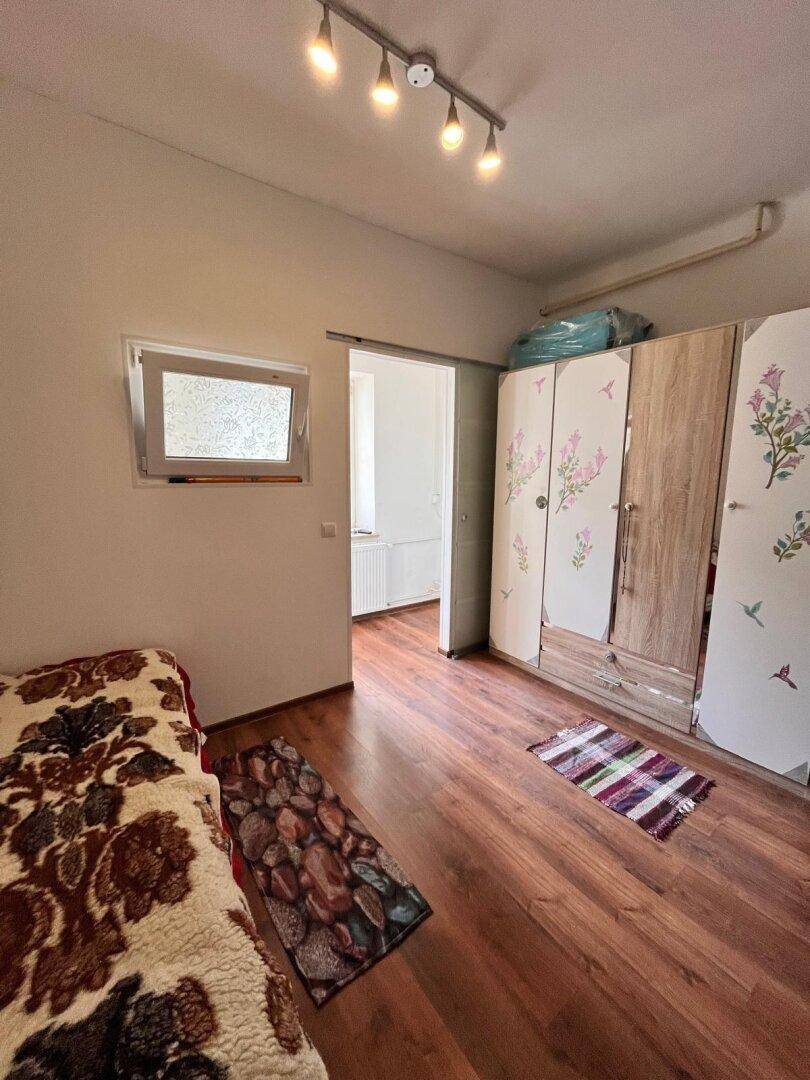 Schlafzimmer mit Laminatboden, Kleiderschrank und einem Bett mit gemusterter Decke.