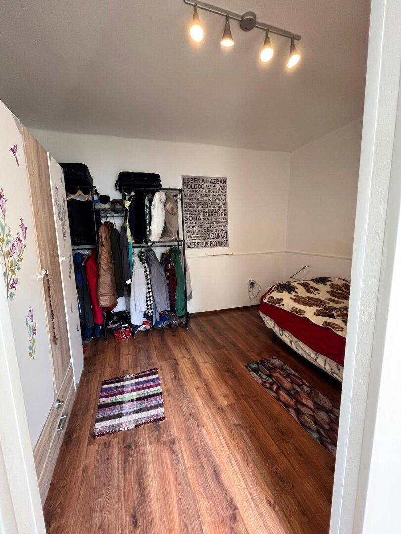 Schlafzimmer mit Laminatboden, Kleiderstange und einem Bett mit gemusterter Decke.