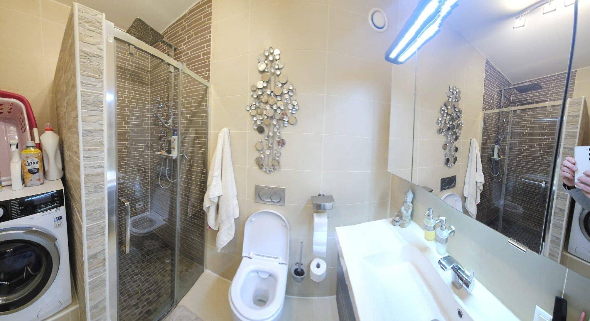 Helles Badezimmer mit Dusche, WC, Waschtisch und integrierter Waschmaschine.