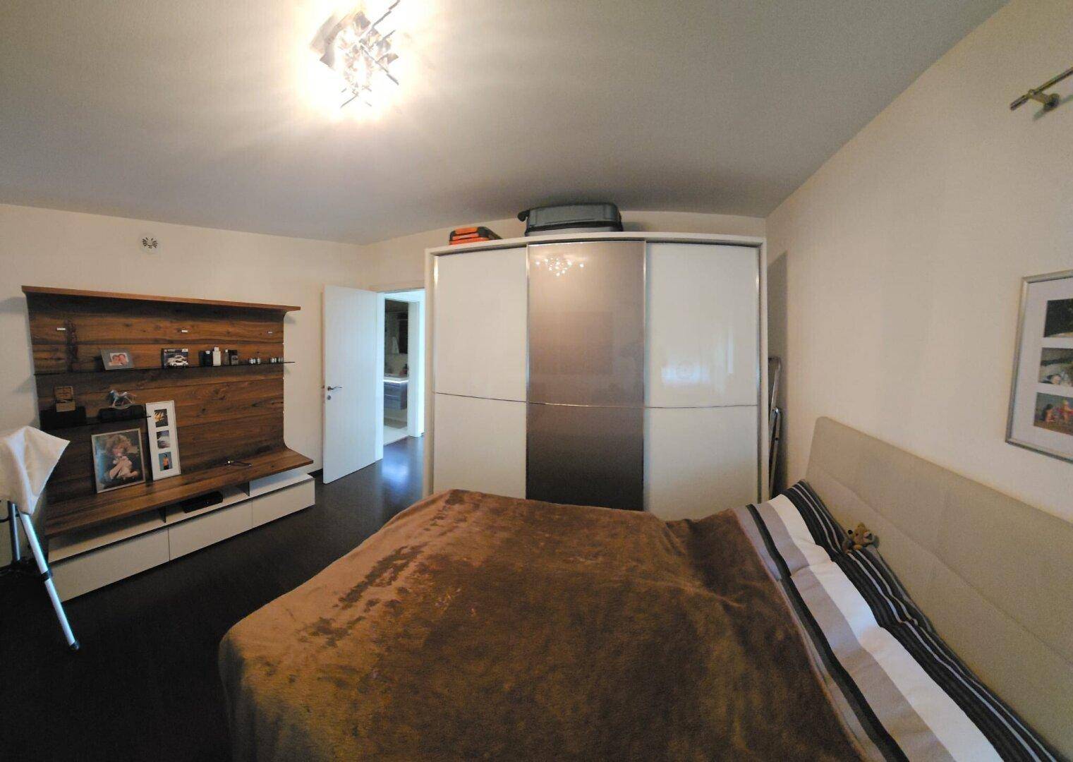 Schlafzimmer mit großem Bett, Schiebetürenschrank und Holzwanddekoration.