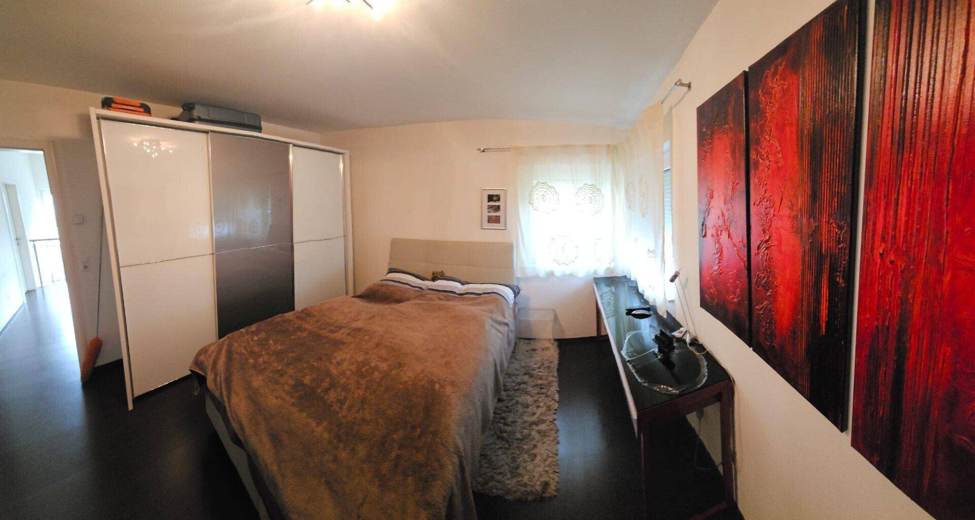 Geräumiges Schlafzimmer mit großem Kleiderschrank, Holzboden und moderner Kunst.