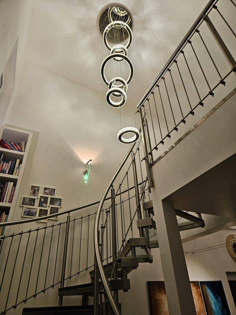 Elegante Wendeltreppe mit Metallgeländer und moderner Hängeleuchte in einem hohen Raum.
