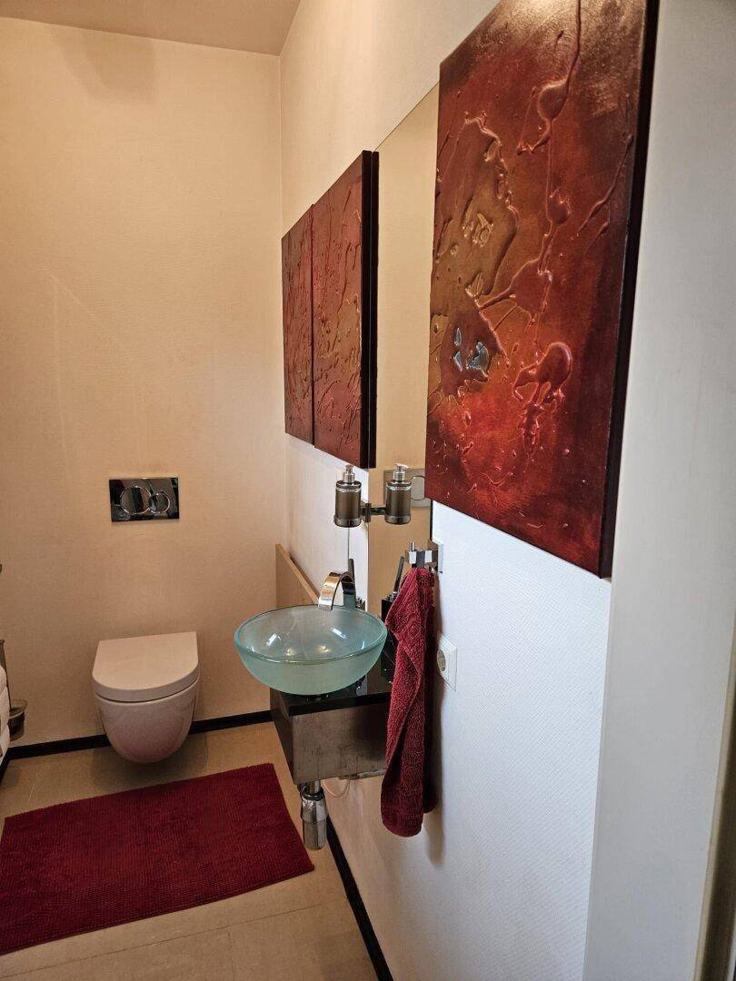 Modernes Gäste-WC mit Wand-WC, Aufsatzwaschbecken und künstlerischer Dekoration.