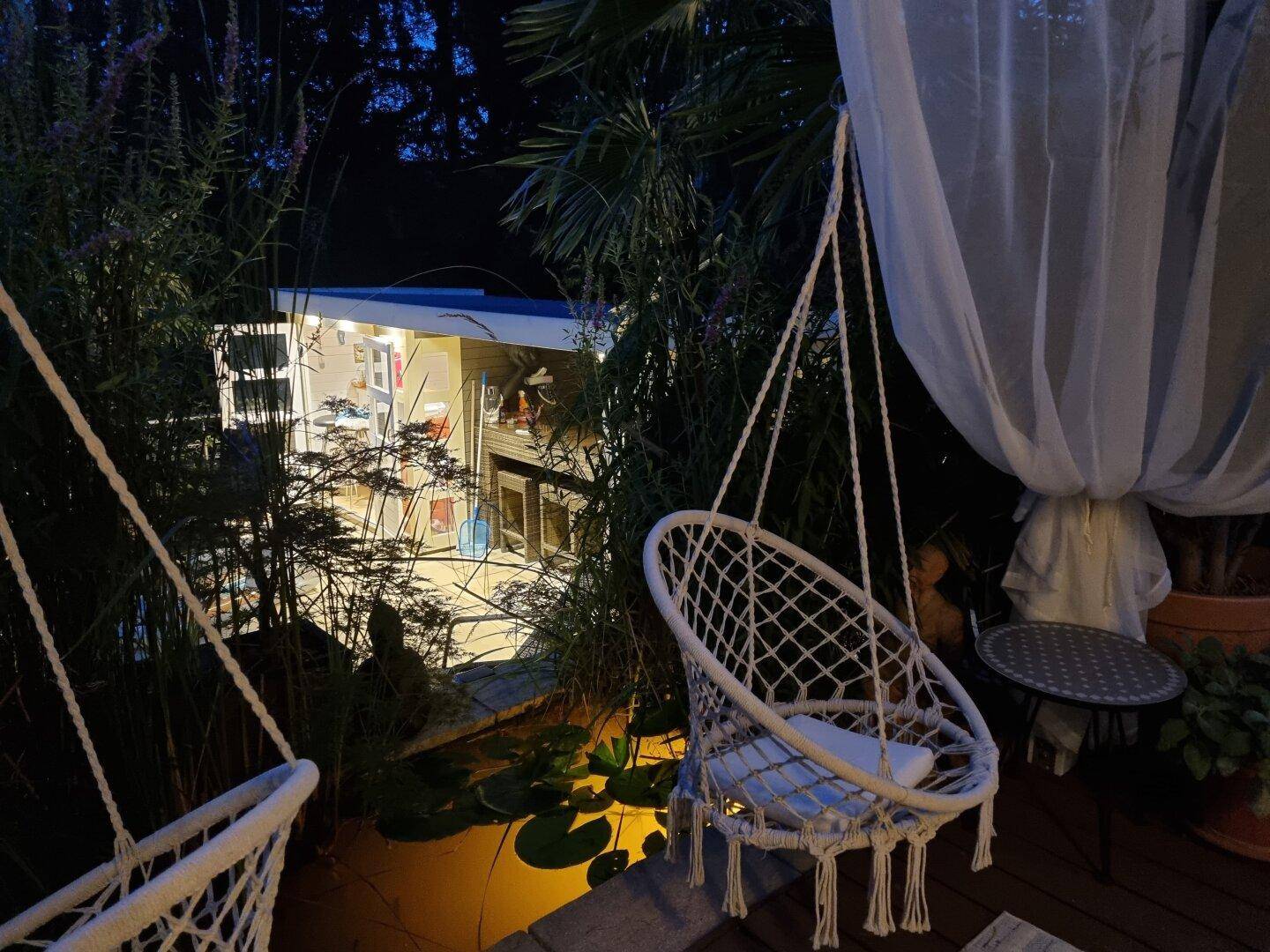 Romantischer Gartenbereich bei Nacht mit Hängesesseln und stimmungsvoller Beleuchtung.