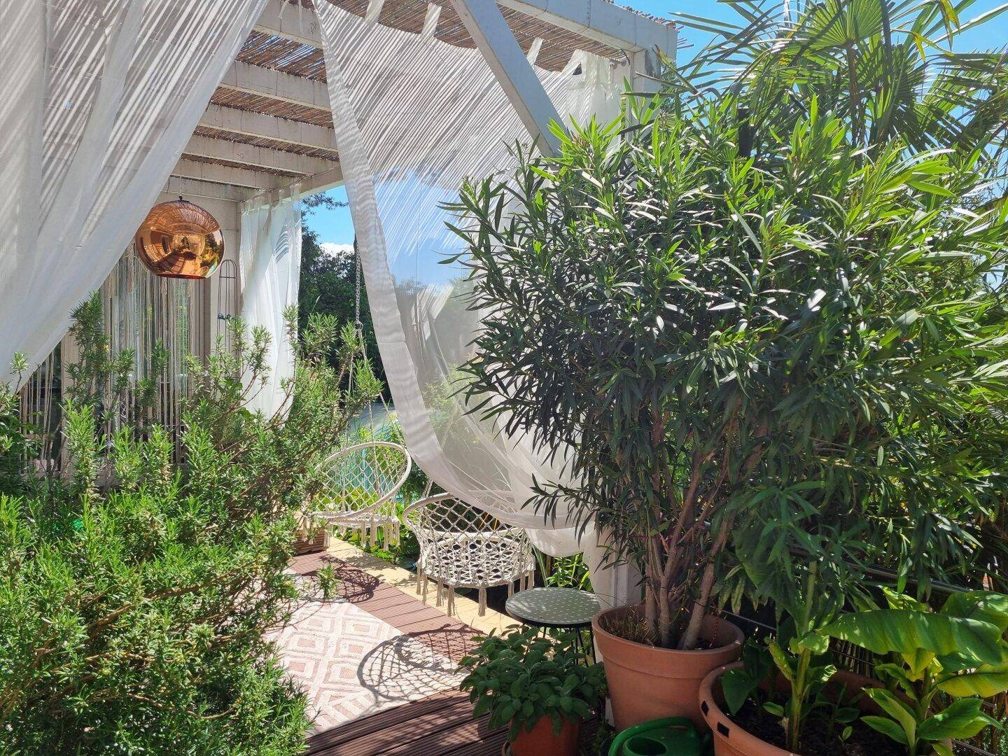 Sonniger Terrassenbereich mit Pergola, Hängesesseln und mediterraner Bepflanzung.
